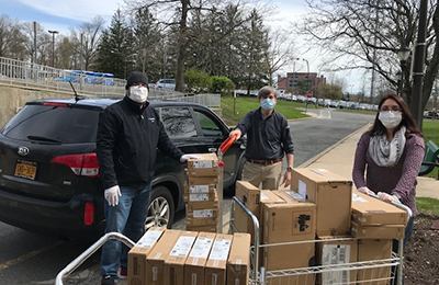 Three people wearing masks and winter clothing are standing outside with boxes of emergency supplies.