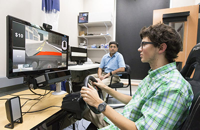 Image of a young man playing on a simulation device while a person looks on.