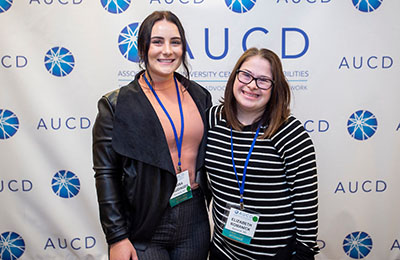 Two woman standing in front of the AUCD Banner.