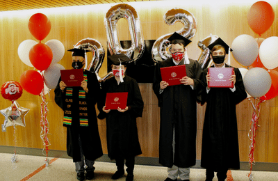 Four young adults dressed in caps and gowns holding up their degrees.