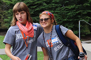 Two college students wearing tshirts and lanyards standing together outside.