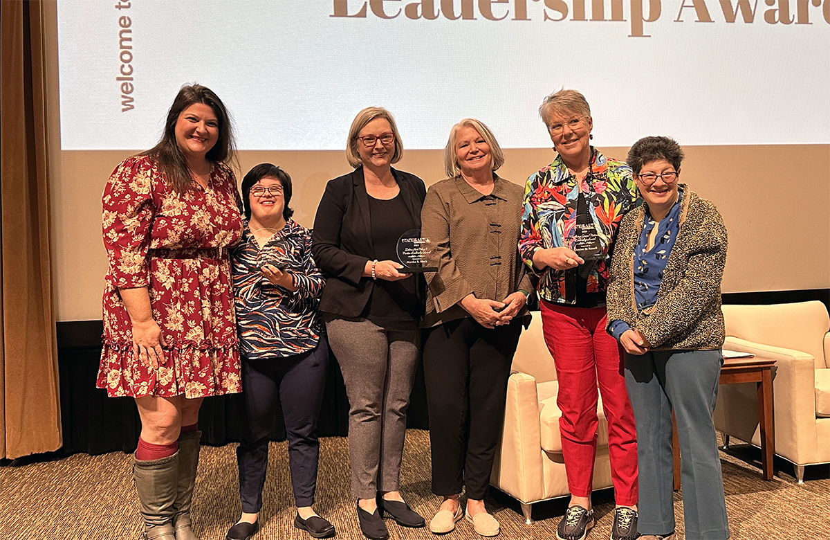 Group of six women, two holding awards standing next to each on a stage.