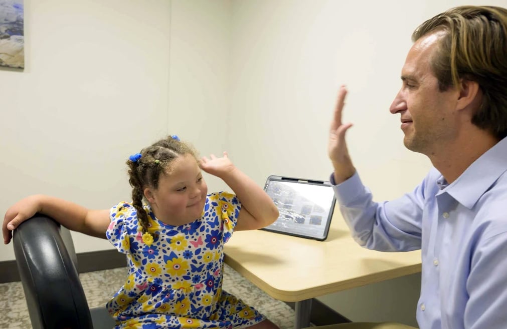 Alt text for photo: Dan Combs, MD high fives young girl with down syndrome in patient room.