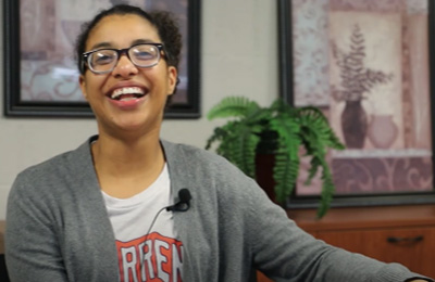 Candace Cunningham is a young black woman with her hair pulled back. She is wearing glasses, a sweater, and a T-shirt.