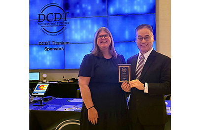 Dr. Zhang, an asian middle aged man wearing glasses and a suit and holding an award and standing next a woman wearing a dress.