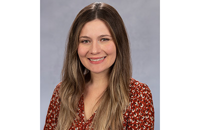 Dainelys Garcia, a hispanic woman with long brown hair, she is wearing a blouse. 