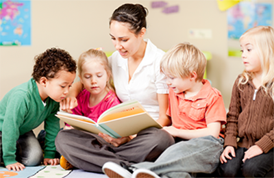 Image of a teacher read a book to her students who are sitting around her.