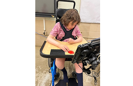 Jaclyns son with his wheel chair tray with an  embedded switcht on his AAC devic