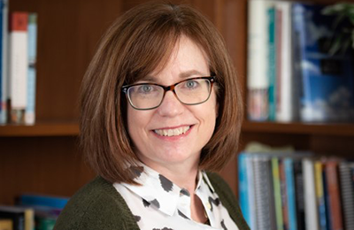 Photograph of Dr. Ronda Jenson, a white woman with shoulder length brown hair wearing glasses and a suit.