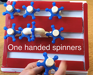 A person tries out a white and blue "one-handed spinner." Several spinners are sitting on a red base.