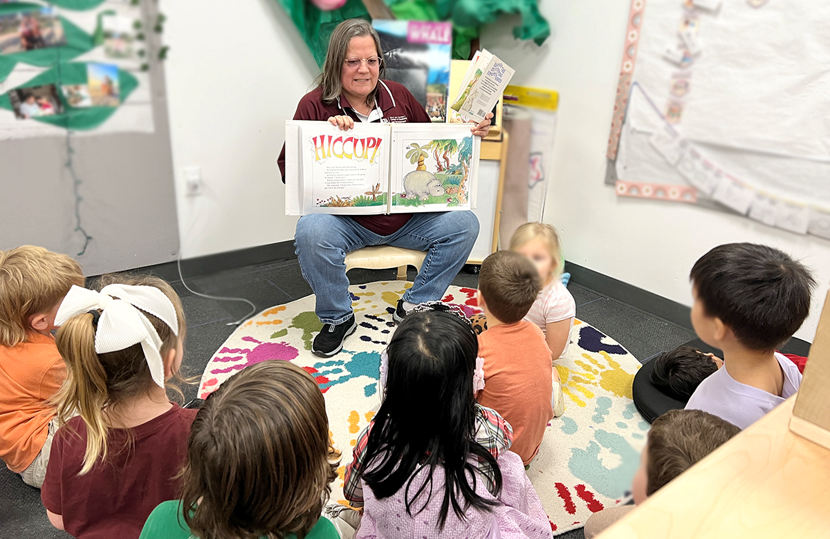 A woman reading a book to children in a classroom.