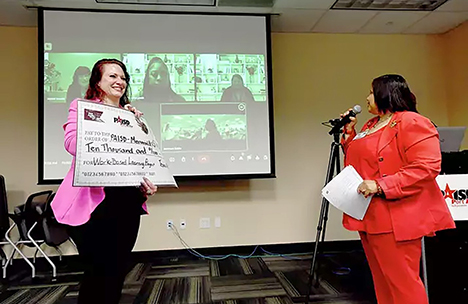 Transition Coordinator Germain Jackson Eddie speaks as teacher Shannon Copley holds up a copy of the ceremonial check awarded to the Titans in Transition 18+ program