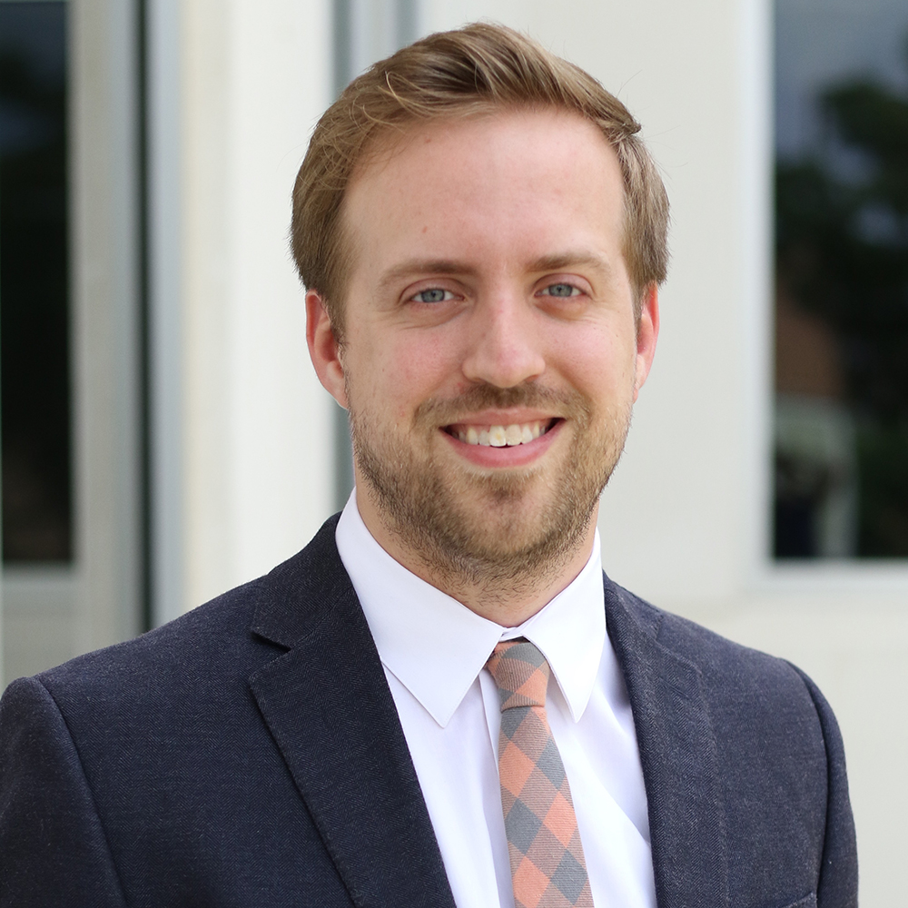 Image of Brad Thomas, a white man smiling wearing a red and white checked polo-button-up shirt.