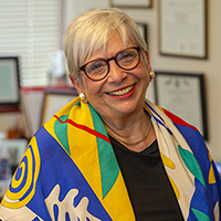 Image of Deborah Spitalnik, a white woman with short grey hair wearing a colorful shall.